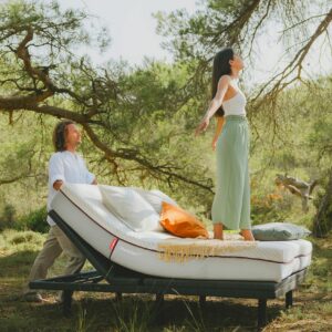Woman standing on top of an adjustable bed & mattress while in the middle of a lush forest.